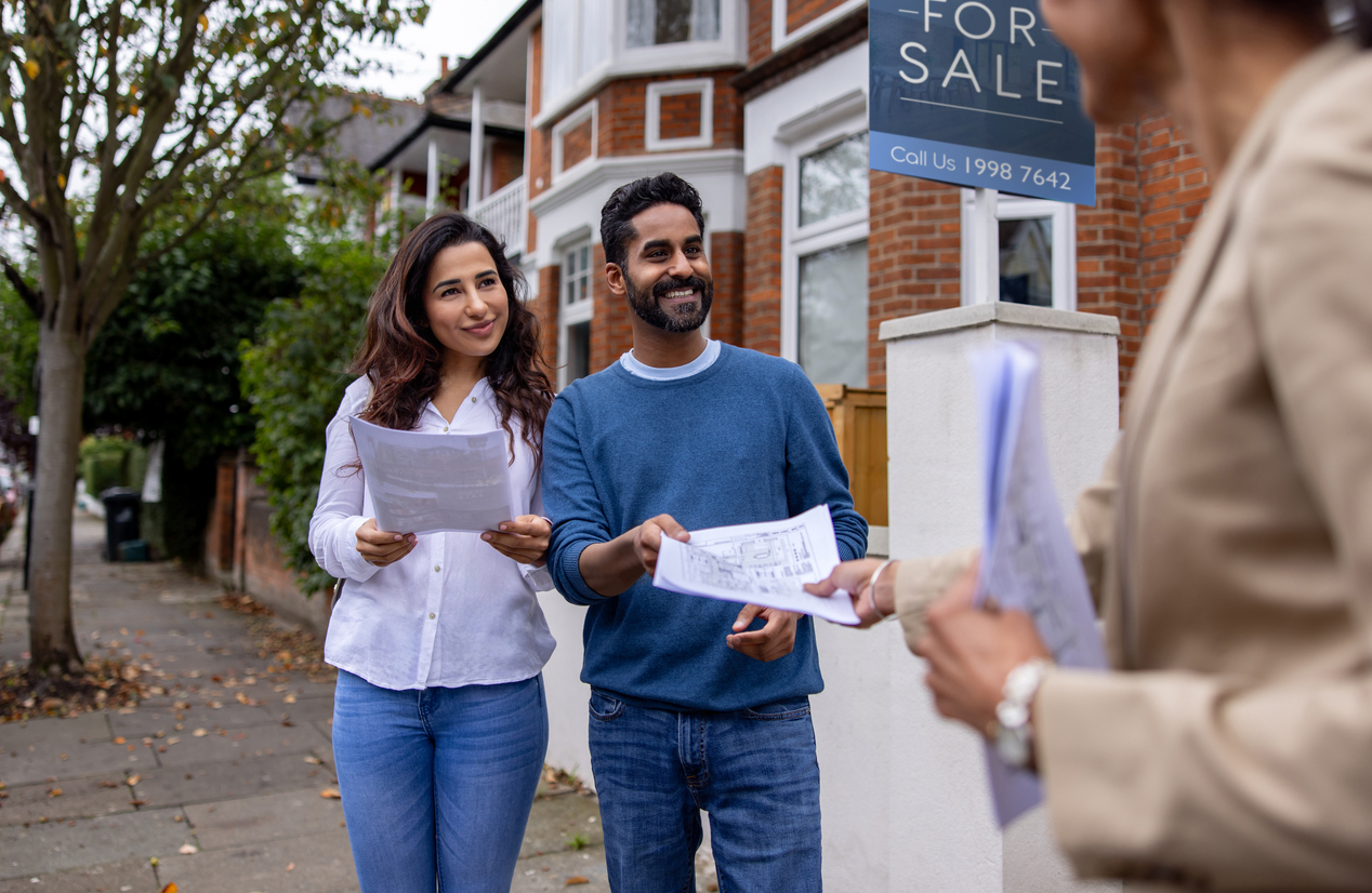 Real estate agent handling the blueprints of a house for sale to a couple